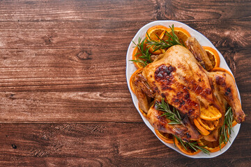 Roasted or baked whole chicken with rosemary and oranges, homemade for Christmas traditional family dinner on an old wooden rustic table. Top view with copy space.