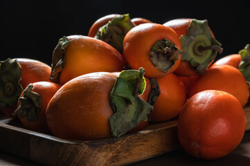 Ripe orange persimmons. Fresh persimmon on a wooden board. Persimmons on a dark background.Selective focus.