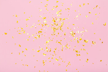 Golden glitter confetti sparkles on pastel pink background. Holiday, festive, party backdrop. Flat lay, top view, copy space.