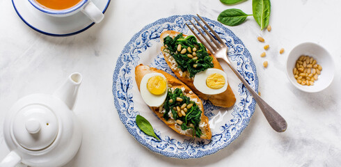 Fried spinach, egg and pine nuts sandwiches or bruschetta on light background. Delicious healthy breakfast or snack. Top view