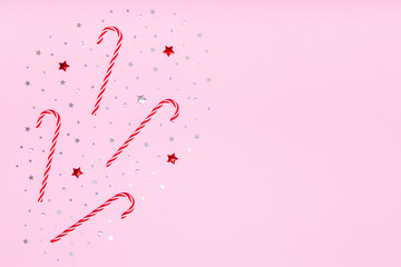Christmas flat lay. Christmas candy canes, red and silver glitter confetti stars on pastel pink background. Flat design, top view, copy space
