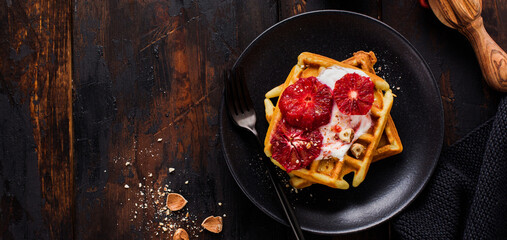 Waffles with yogurt and red Sicilian orange sauce on old dark wooden background. Top view