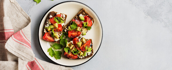 Avocados, cherry tomatoes and feta cheese sandwiches with balsamic sauce and cilantro on old olive board. Top view