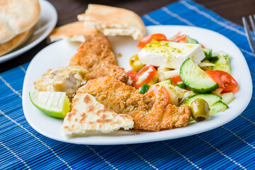 Baked fish served with vegetable salad with feta cheese
