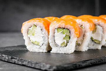 appetizing philadelphia sushi roll with salmon and cucumber on a black stone plate