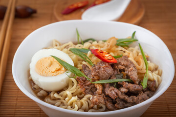 Ramen soup with chicken, noodles, egg, hot pepper and sprouted beans in a white plate against a mat with a spoon and chopsticks. Asian street food.