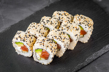 appetizing california sushi roll with cheese avocado cucumber and salmon in sesame seeds on a black stone plate