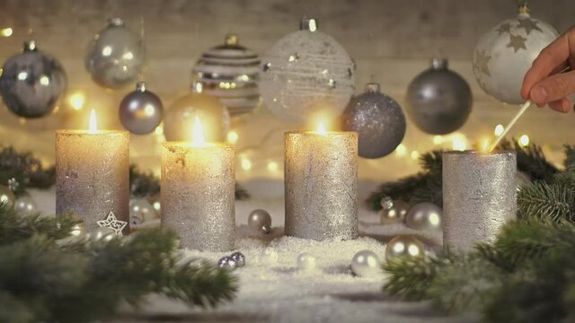 Footage of elegant advent decoration with fir branches on snow and fourth candle being lit, with lights and baubles hanging in the background