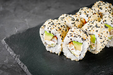 appetizing sushi roll california with eel avocado cucumber and sesame seeds on a black stone plate