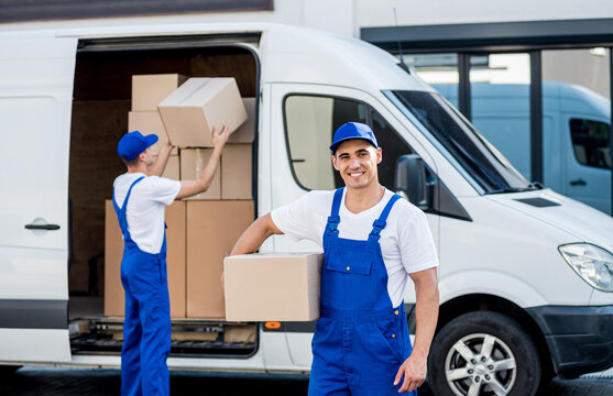 Two removal company workers unloading boxes from minibus into new home