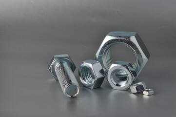 composition of new bolts and nuts of different sizes on a gray background.