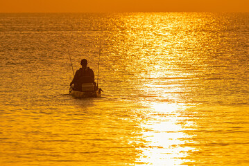 Naklejka na ściany i meble A man is fishing on a small boat in the bright morning light.