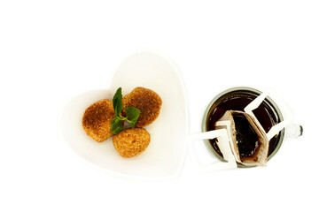 Three balls of cheese bread placed inside a heart-shaped bowl next to glassware cup with filter to make American coffee Brazilian breakfast
