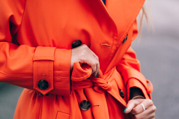 Fashionable blonde woman wearing orange coat, blue jeanse , white sneackers and neckchain posing in...