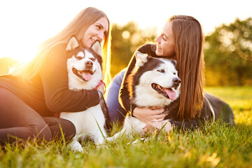 Millennial girls playing with their siberian husky dogs outdoors in the grass - Cheerful young owners and their pets having fun together in the garden - Dog and human frinedship concept