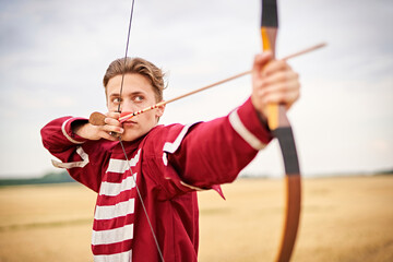 Young male sportsman targeting with bow in a traditional, medieval archer costume - Teenager archer...