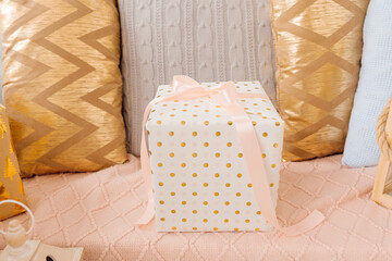 gift box wrapped in white gift paper with golden peas tied with pink ribbon on bow stands on pink background. Delicate pillows, surprise, gift concept
