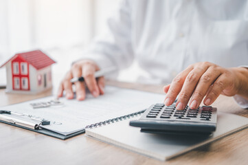  woman calculates her budget before signing a real estate project contract with a house model.