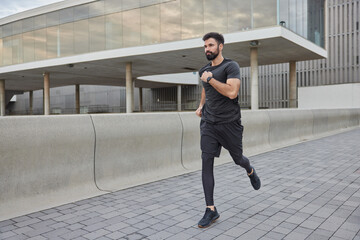 Athletic bearded adult man runner enjoys jogging in city demonstrates endurance dressed in...