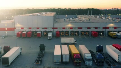 Semi-trailer truck is travelling along a logistics warehouse with a lot of ramps for loading and unloading goods. Aerial side view