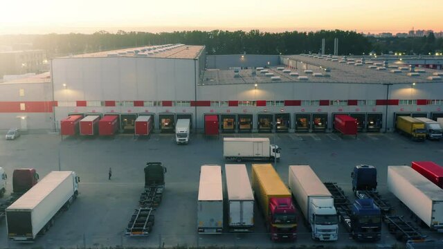 Semi-trailer truck is travelling along a logistics warehouse with a lot of ramps for loading and unloading goods. Aerial side view
