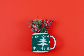 A mug in a green sweater with fir branches and lollipops candy, lie in the middle on a red