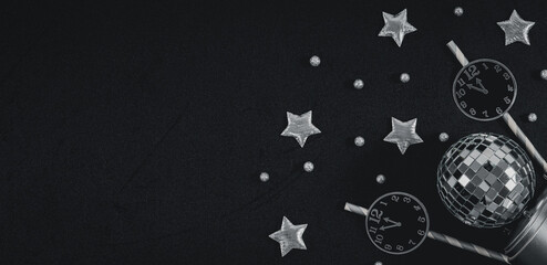 Paper clock on straws, silvery stars, disco ball and snow ball on black background.