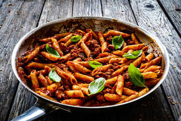 Penne with minced meat, tomato sauce, parmesan cheese, basil and vegetables served in frying pan on...