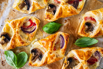 Baked puff pastry with mozzarella, white mushrooms and red bell pepper on baking paper

