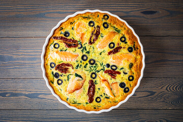 Millet quiche with salmon, spinach and black olives in cooking pan on wooden table
