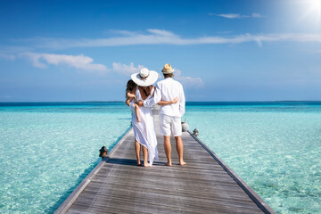 A family in white summer clothes stands on a wooden pier over turquoise sea in the Maldives islands during their vacation time