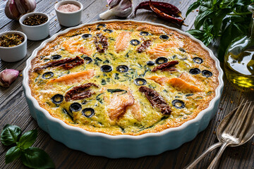 Millet quiche with salmon, spinach and black olives in cooking pan on wooden table

