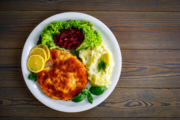 Breaded fried pork chop with potato puree, beetroots, lemon and fresh vegetables on wooden table

