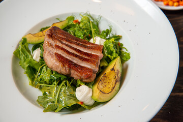 duck steak with fresh vegetables and avocado on a white round plate on a wooden table