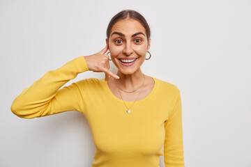 Obraz premium Photo of happy young European woman shows mobile phone call me gesture invites you and asks to contact her wears casual yellow jumper isolated over white background. Give me call sometimes please