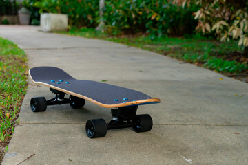 A black Surf Skate has a black top and black wheels resting on a cement floor in a garden.