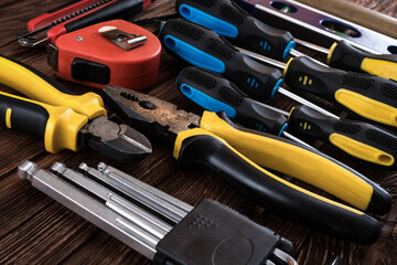 Locksmith's working tool. Mechanical assembly and disassembly tool. Screwdrivers, pliers, wire cutters, building level, tape measure, hammer, wrenches, square and other tools on a wooden surface.