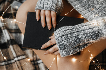 Close up shot of womans hands holding a book and fairy lights.