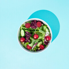Food creative healthy fresh salad made of cucumber, cabbage, lettuce and red decoration Christmas ball as  Cherry tomato. Vegetarian New year concept. Flat lay on pastel blue background...