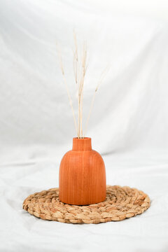 minimalist setting of product platform shot for showcasing a rustic vase with dried plant in it. the arrangement of wooden vase on the wicker placemat.