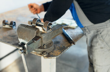 A worker in overalls works behind a workbench with metal vises. Production of metal parts at the factory. Equipment assembly.
