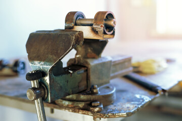 The metal product is squeezed in a vice at the workplace in the workshop. Workbench with old vises.