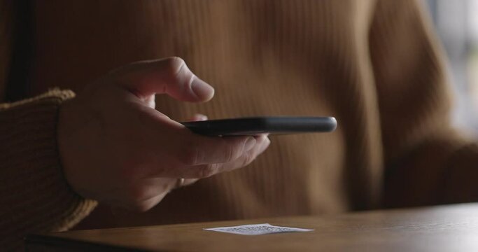 Close-up of smartphone in male hands tapping on screen. Man scanning QR code on table in restaurant or cafe. Online menu for clients. Convenience, contactless concept.