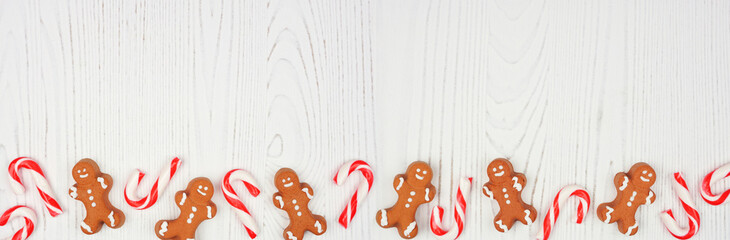 Christmas bottom border of gingerbread cookies and peppermint candy canes. Top view on a rustic white wood background with copy space.