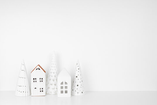 White Christmas Decor On A White Shelf Against A White Wall Background With Copy Space. Ceramic Trees And Village Houses.