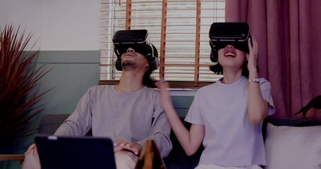 Asian couples wearing modern Virtual reality glasses sit and watch movies in living room at home. Holiday Activity family entertainment technology. living together happiness. Concept metaverse - Powered by Adobe