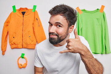 Handsome bearded adult man makes call me gesture asks for telephone number dressed in casual t...