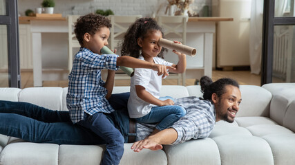 Happy African American daddy and little sibling kids playing funny active games on couch, Children...