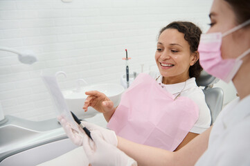 Focus on woman patient in a dentists chair looking at the panoramic dental X-ray while dentist hygienist explains the consultation treatment issues. Concept of medical diagnostics in dental practice