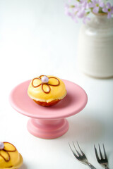 Yellow petit four on a lilac cake stand. Vase with lilac flowers